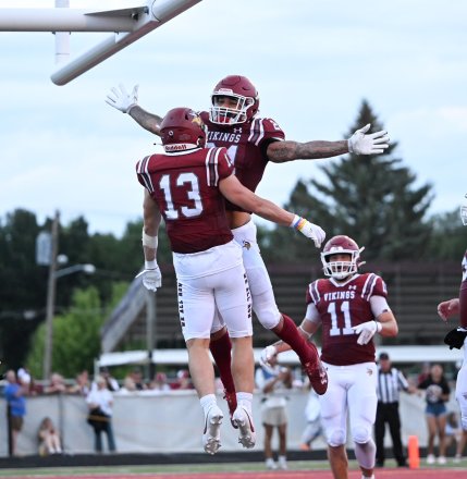 Two VCSU football players celebrate a touchdown with a leap in the endzone.