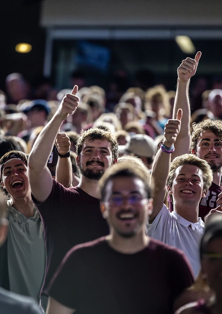 A crowd cheering and throwing up thumbs ups