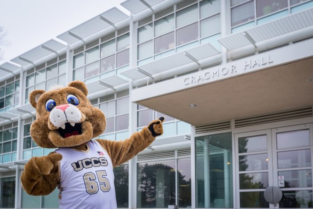 Clyde, the UCCS Mountain Lion Mascot, pointing to the entrance of Cragmor