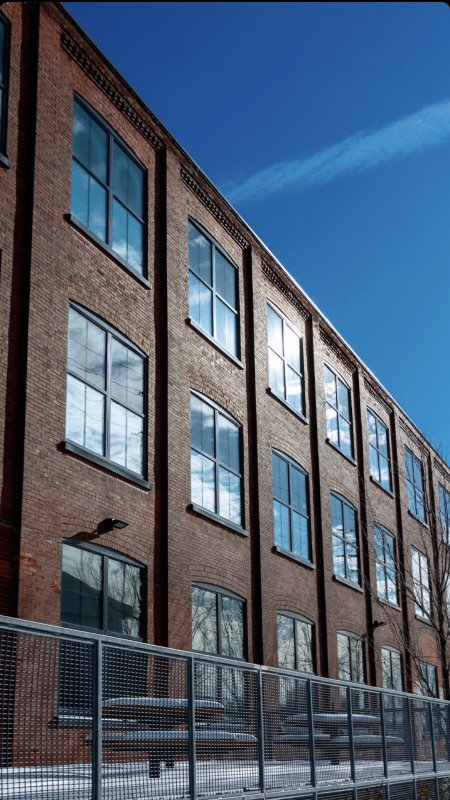 Exterior view of Charles Hall, an old brick building with 3 floors full of windows that are reflecting the sky.