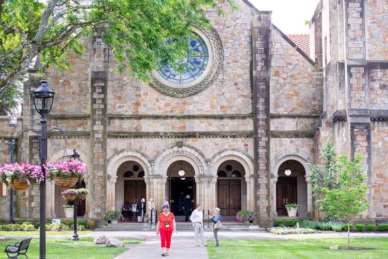  A woman strolls along the sidewalk, passing by a beautiful church in the background.