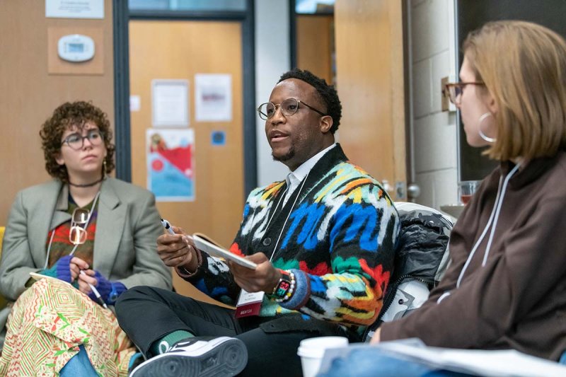  A mentor sits in a chair surrounded by two other people, engaged in a lively discussion.