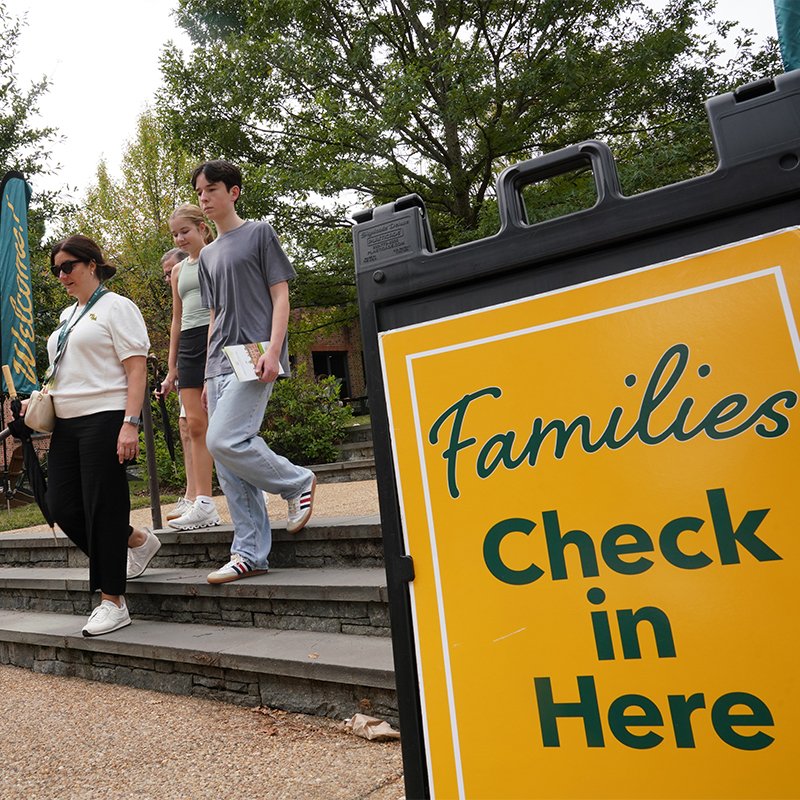 People walking down the stairs with a sign that reads "Families Check In Here" in the foreground.