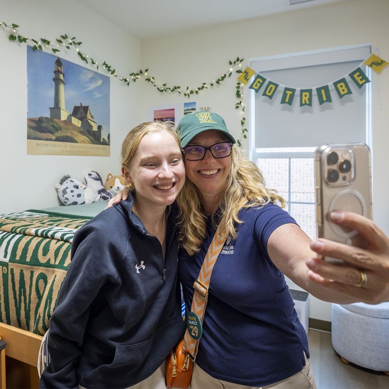 A parent and their student take a selfie inside of a decorated dorm room.