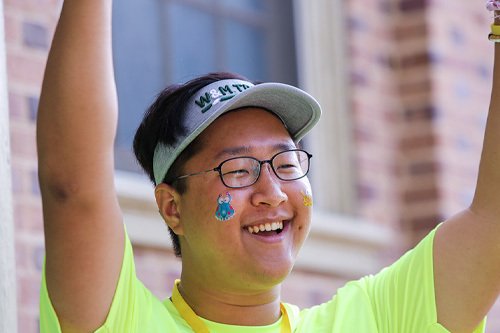 A smiling student greeting students as they arrive.