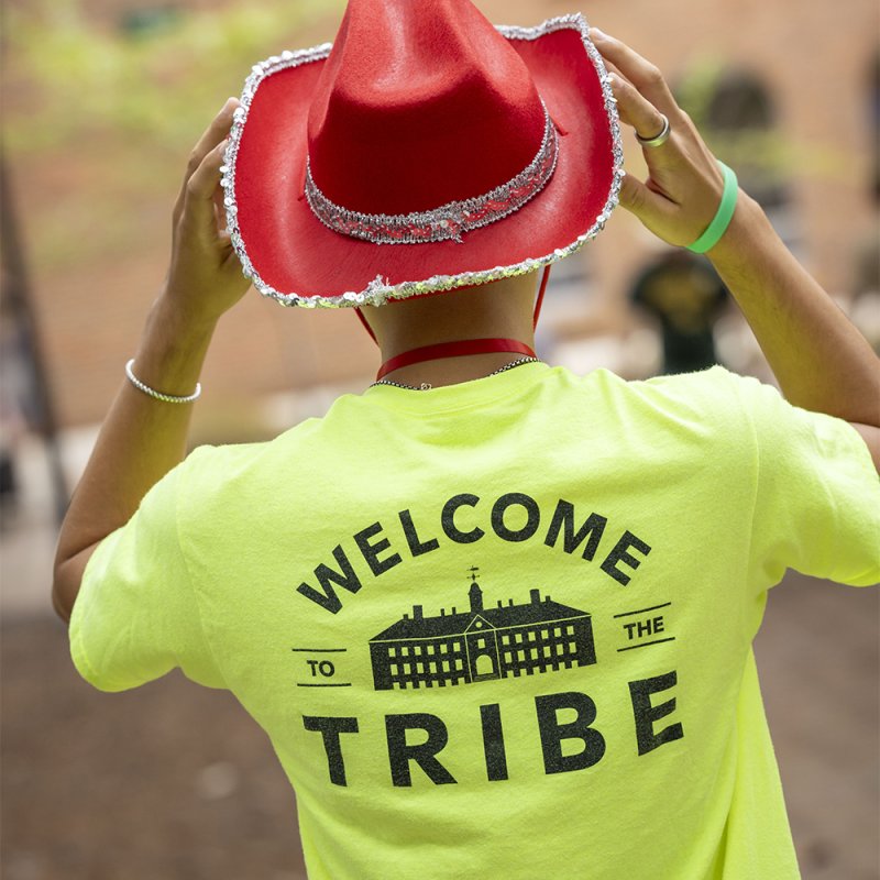 A student in a bright yellow &ldquo;Welcome to the Tribe&rdquo; T-shirt adjusts a red cowboy hat.
