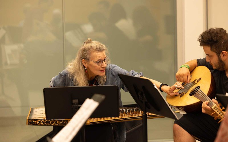 A professor giving lessons to a student who is using a stringed musical instrument.