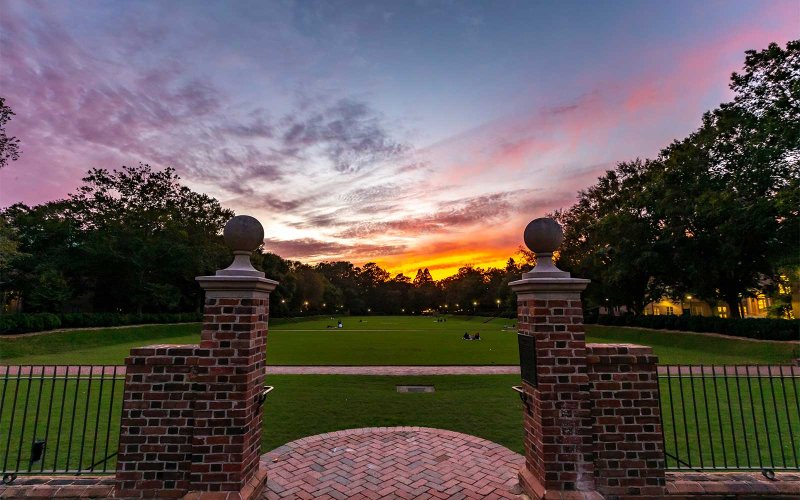Sunset view of the Sunken Garden framed by brick pillars with people on the lawn.