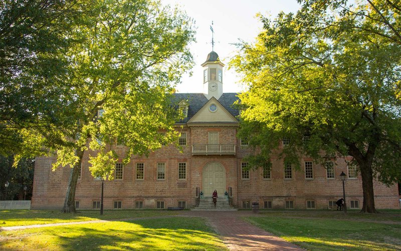 Front view of the Wren Building with trees framing the entrance and a person on the steps.